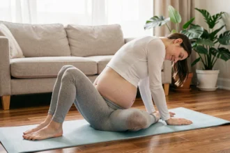 Femme enceinte pratiquant un étirement doux de yoga sur un tapis bleu pour soulager les douleurs lombaires